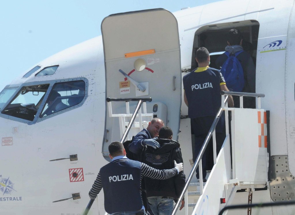 From file: Italian police officers escort migrants onto an airplane in Lampedusa, Italy | Photo: EPA/Carlo Ferraro