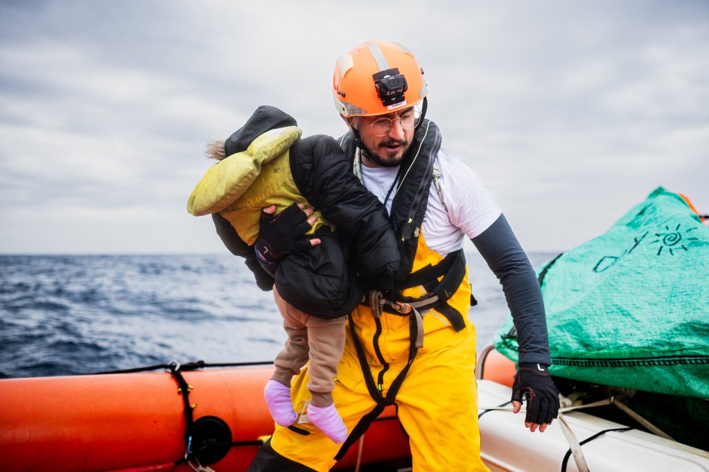 A crew member of the “Ocean Viking” rescue ship carries a young child on their RHIB (Rigid inflatable boat) during a rescue operation in the search-and-rescue zone off the international waters of Libya, on January 16, 2026 | Photo: Sameer Al-Doumy, AFP