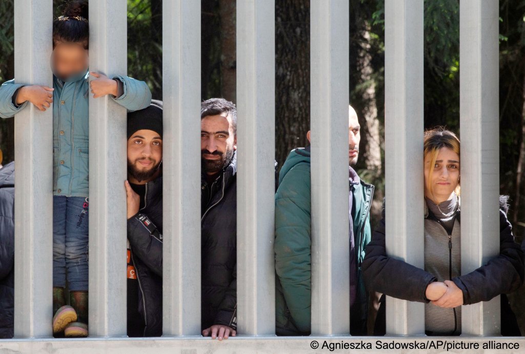 Members of a group of some 30 migrants seeking asylum are seen on Sunday, 28 May 2023 across from a wall which Poland has built on its border with Belarus | Photo: Agnieszka Sadowska/AP