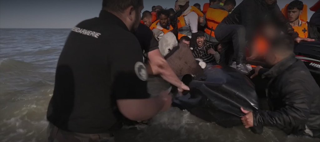 A screenshot from a BBC video published on July 4, 2025, shows French officers intervening in shallow waters and puncturing a boat with a knife to prevent it from leaving the shore | Source: BBC News