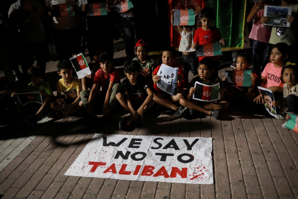 On August 16, 2021 children on the Greek island of Lesbos sit in front of a banner reading "We say No to Taliban" as Afghan migrants demonstrate against the Taliban takeover of Afghanistan | Photo: Elias Marcou/Reuters