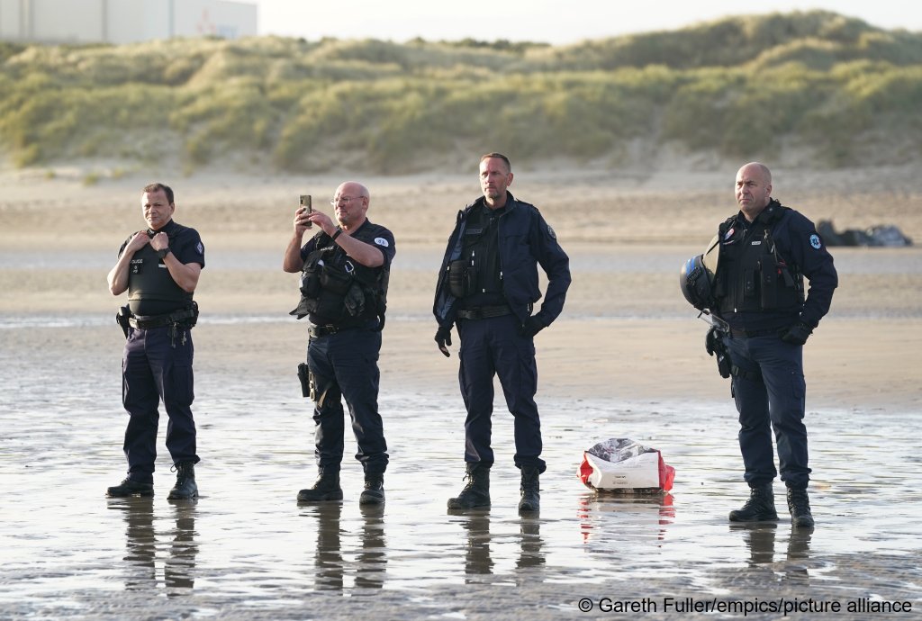 French police officers watch a group migrants board a small boat leaving the beach at Gravelines, France | Photo: Gareth Fuller/empics/picture-alliance