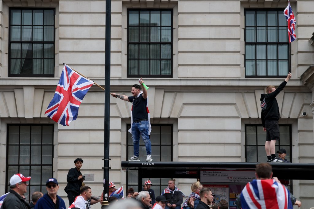 File photo: Protesters holding Union Jack flags stand on a bus stop roof during a 'Unite the Kingdom' rally organized by British anti-immigration activist Stephen Yaxley-Lennon, also known as Tommy Robinson, in London, Britain, May 16, 2026 | Photo: Hannah McKay / Reuters