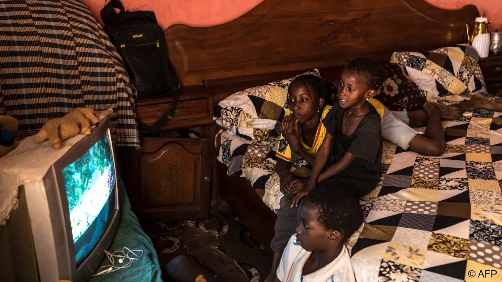 Sokhna (L), Coumba (C) and Boubacar (R) watch TV at their home in Mbour, on March 9,2026. The three siblings lost their father in 2022 as the pirogue he was traveling in capsized trying to reach Europe through the Atlantic route | Photo: Patrick Meinhardt / AFP