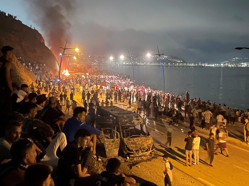 Migrants gather around a torched vehicle while waiting for a chance to cross to the Spanish enclave of Ceuta, on the Moroccan side of the border in Fnideq, Morocco, July 31, 2026 | Photo: Ahmed El Jechtimi / Reuters