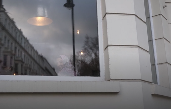 An Afghan woman sits in the window of the hotel accommodating refugees in London | Photo: Screenshot from DW report / DW / Kate Martyr