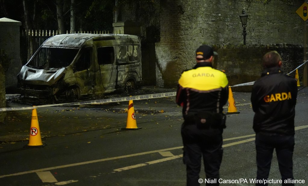 Police stand next to a burned out van in Dublin following violence | Photo: Niall Carson / PA Wire / picture alliance