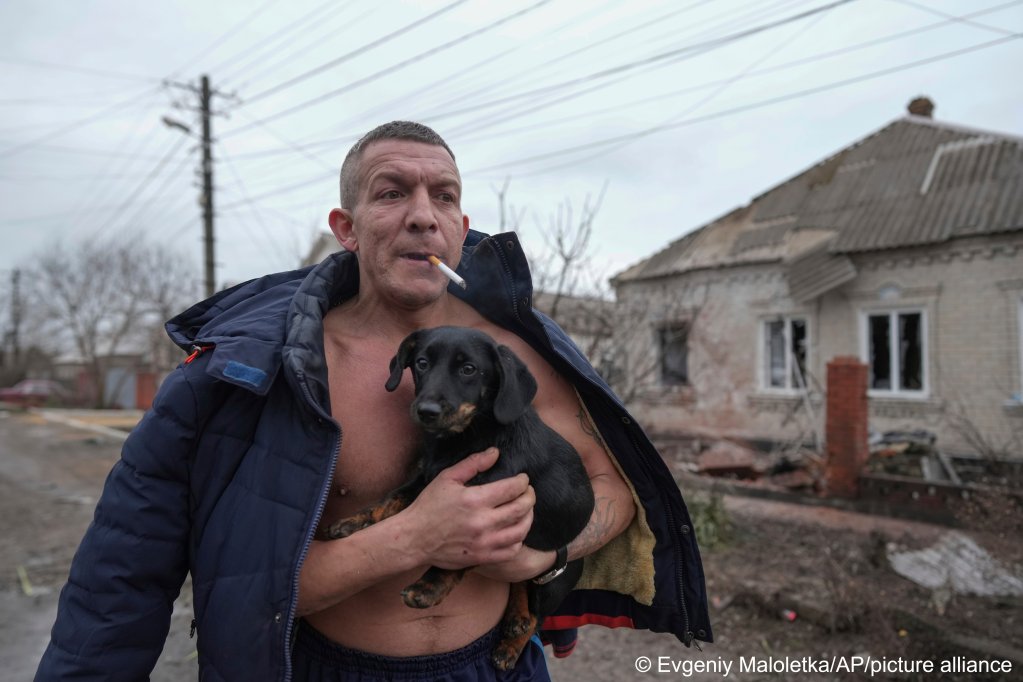 A man holds a dog as he walks past a damaged house following Russian shelling in Mariupol, Ukraine, on February 24, 2022 | Photo: Evgeniy Maloletka/AP/picture alliance