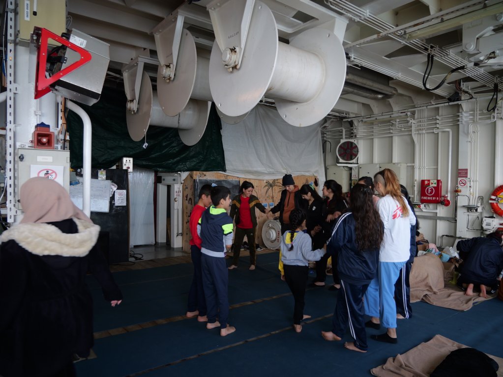 Migrants on board the Geo Barents perform a Kurdish dance, teaching an MSF worker some traditional dance moves | Central Mediterranean Sea, February, 2024 | Photo: Sou-Jie van Brunnersum
