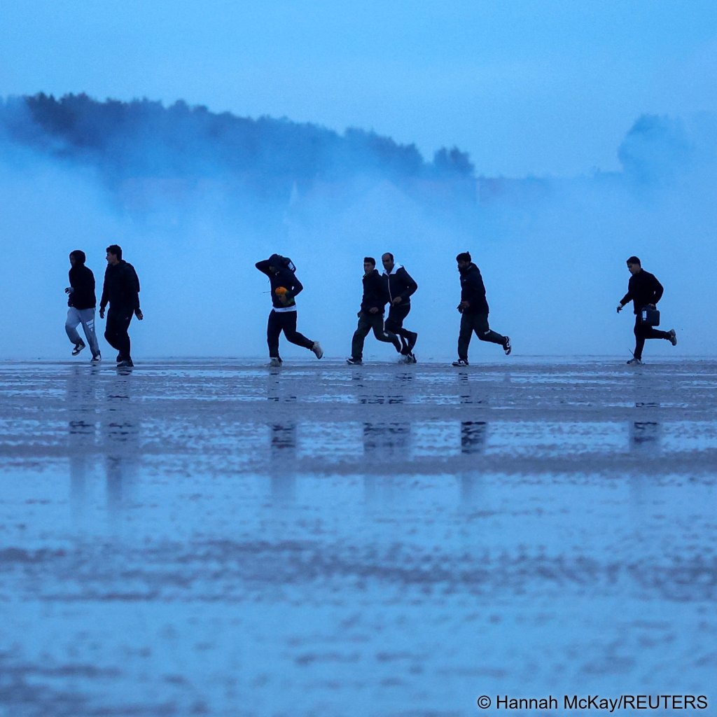 Migrants run away from tear gas fired by police as they try to leave the coast of northern France in an attempt to cross the English Channel to reach Britain, from the beach of Petit-Fort-Philippe in Gravelines, near Calais, France, September 28, 2026 | Photo: Hannah McKay / Reuters