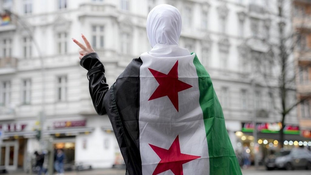 File photo: A Syrian woman making the victory sign and flying a Syrian opposition flag in the streets of Berlin, December 10, 2024 following the fall of the Assad regime | Photo: Ebrahim Noroozi/AP