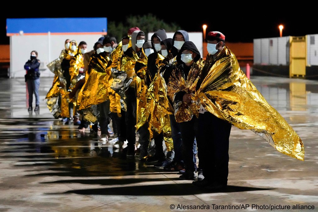 Migrants wrapped in space blankets wait on the quay after disembarking in the port of Roccella Jonica, Calabria region, southern Italy, early Sunday, Nov. 14, 2021 | Photo: Alessandra Tarantino/AP/picture-alliance