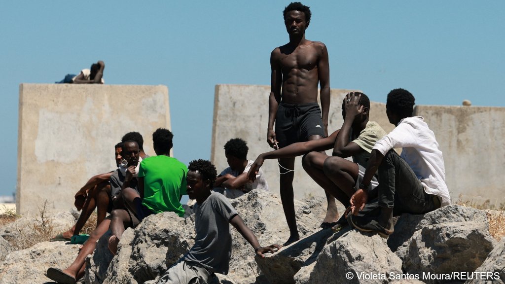 Migrants wait at a breakwater on a beach in Ceuta, Spain, following deadly mass crossings of migrants on foot and by sea from Morocco into Spanish territory, August 4, 2026 | Photo: Violeta Santos Moura / Reuters