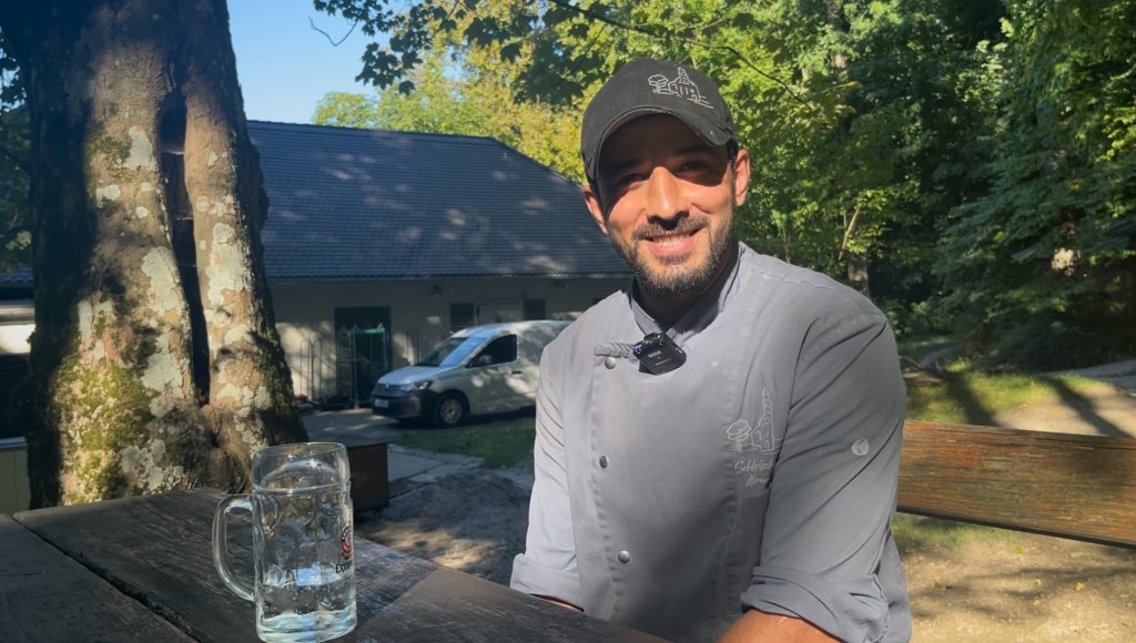 Chef Hassan Hedayati sitting at a table in the Mariabrunn beer garden. | Photo: Natasha Mellersh / InfoMigrants