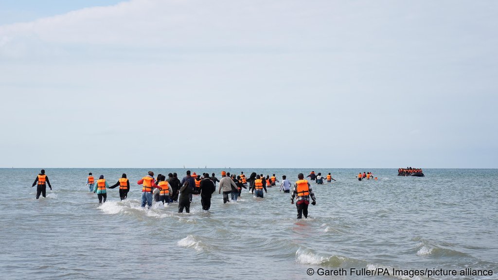 Dozens of people running towards a crowded dinghy already carrying dozens of people, off the coast of Equihen-Plage, France, on July 22, 2026 | Photo: picture alliance