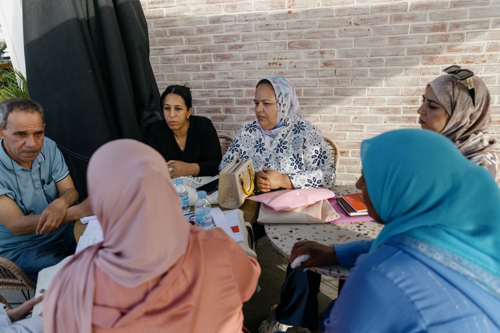 Hafida (en noir), Fatima (haut à fleurs bleues) assises aux côtés de Hassan, président de l’Association Marocaine d’Aide aux Migrants en Situation Vulnérable (AMSV), créée en 2017 et basée à Oujda. En face d'eux trois, d'autres représentantes de familles de disparus. Rabat, mai 2026. Crédit : Valentina Camu (Divergence)