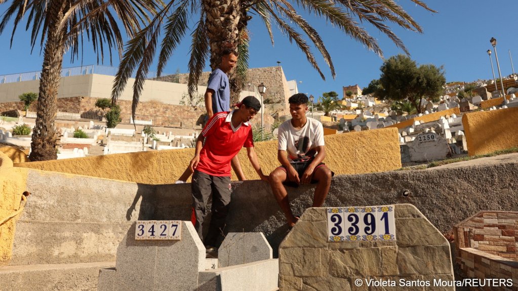 Mohammed, a 22-year-old migrant from Morocco, sits on a wall as others join him at the Sidi Embarek cemetery in Ceuta, where migrants sought refuge after mass crossings on foot and by sea from Morocco into the Spanish enclave, in Ceuta, Spain, August 5, 2026 | Photo: Violeta Santos Moura/Reuters