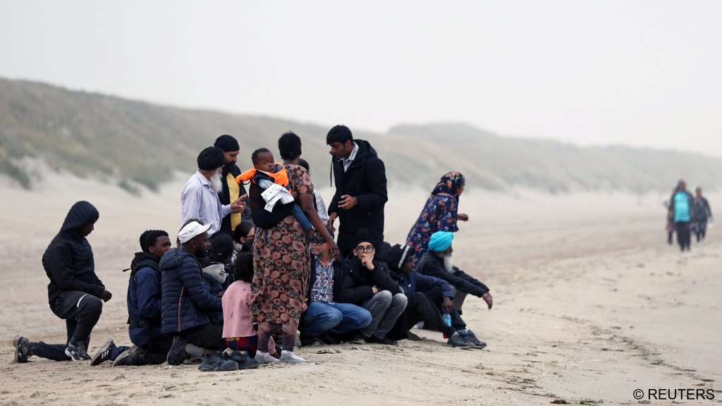 A group of migrants wait on the beach before the arrival an inflatable dinghy in an attempt to cross the English Channel to reach Britain, at the beach of Petit-Fort-Philippe in Gravelines, near Calais, France, July 2, 2025 | Photo: Gonzalo Fuentes / Reuters