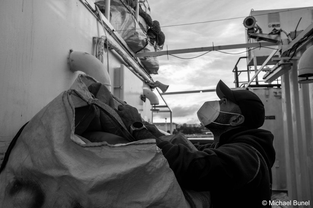 A quai dans le port de Marseille, les équipes préparent le bateau pour le départ. Astoun charge un sac rempli de gilets de sauvetage, le 16 décembre 2022 | Photo : Michael Bunel