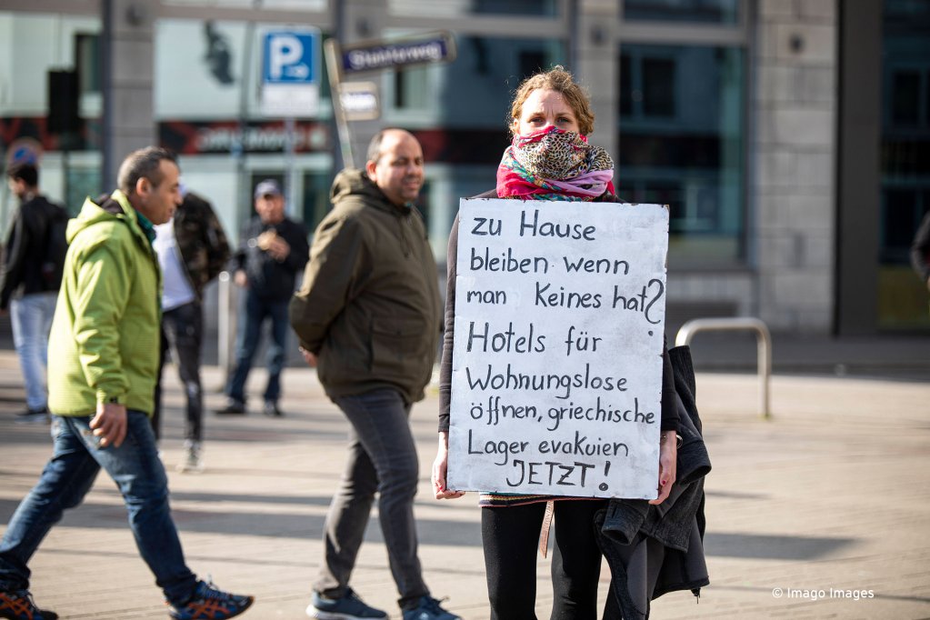 متظاهرة في ألمانيا يحمل لافتة كتب عليها "ابق في المنزل عندما لا يكون لديك شيء لفعله؟ افتح الفنادق للمشردين، وقم بإخلاء المخيمات اليونانية الآن!"