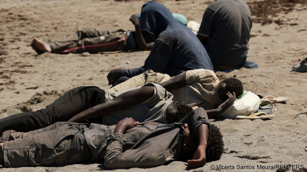 A group of people rest while waiting on a beach following mass crossings of migrants on foot and by sea from Morocco into Spanish territory, in Ceuta, Spain, August 4, 2026 | Photo: Violeta Santos Moura / Reuters