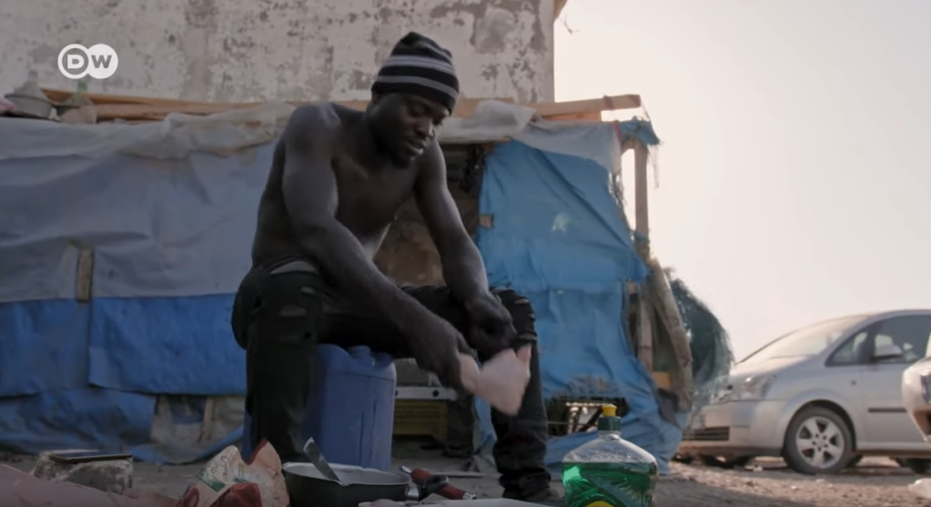 Edward 'King' Owusu prepares a meal for his colleagues when they come home from the fields. He hides his bandaged head under a hat | Photo: Screenshot DW documentary Tomatoes and Greed