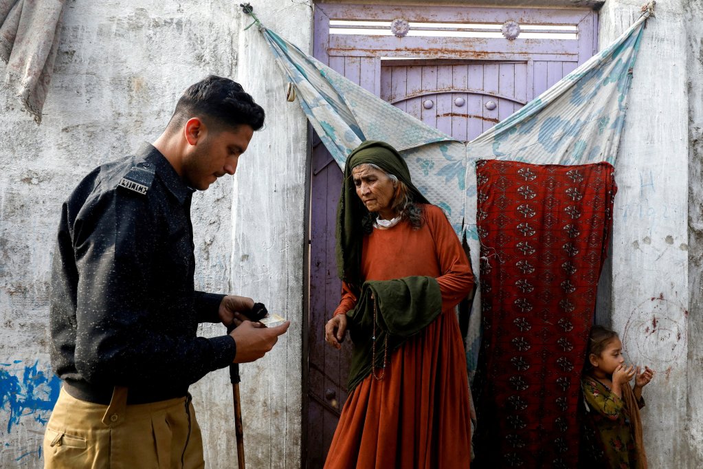 Edema Bibi, 66, an Afghan citizen, stands at the entrance of her house as a police officer checks her registration card, during a door-to-door search and verification drive for undocumented Afghan nationals, in an Afghan Camp on the outskirts of Karachi, Pakistan, November 21, 2023. REUTERS/Akhtar Soomro/File Photo
