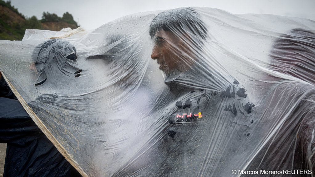 File photo: Migrants shield themselves from the rain while queuing to charge their mobile phones at an NGO stand in Ceuta | Photo: Marcos Moreno/Reuters