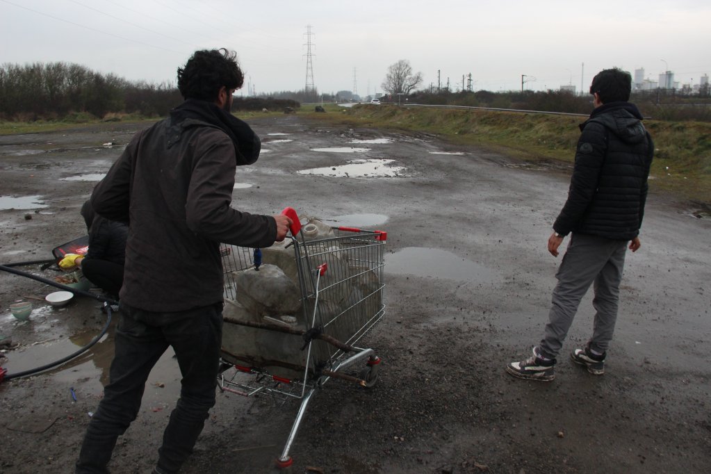 Les exilés doivent parfois marcher près de deux kilomètres à Loon-Plage pour accéder à leur seul point fixe d'eau courante, dont ils remplissent des bidons usagés. Crédit : Arnaud Stoerkler