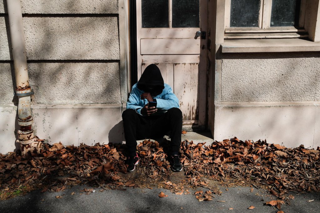 An unaccompanied migrant child checking his phone in the yard of an abandoned school in Paris, France | Photo: Teresa Suarez / EPA