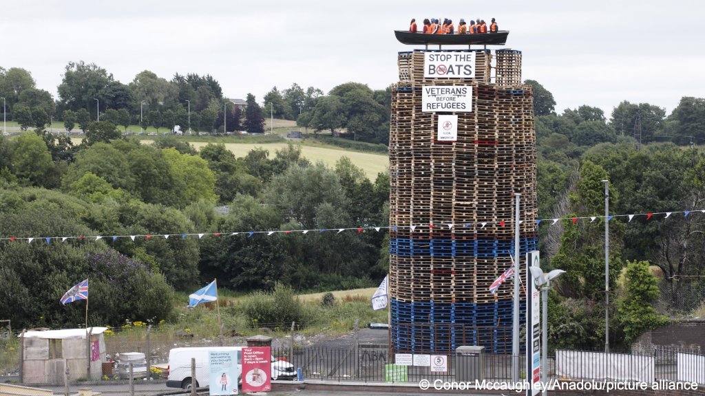 A bonfire structure featuring an effigy of refugees in a boat with banners 'Stop the boats' in Tyrone, Northern Ireland on July 9, 2025 | Photo: Conor<br>Mccaughley/Anadolu/picture alliance