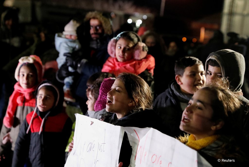 أطفال يحملون لافتات بينما يتجمع المهاجرون على الحدود الصربية المجرية للمطالبة بالمرور إلى الاتحاد الأوروبي، بالقرب من كيلبيجا، صربيا ، 6 فبراير 2020.