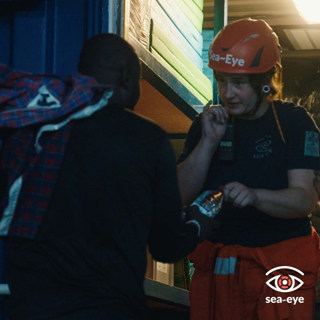 A member of the Sea-Eye 4 crew welcomes one of the migrants on board the ship with a bottle of water | Source: X feed @seaeyeorg