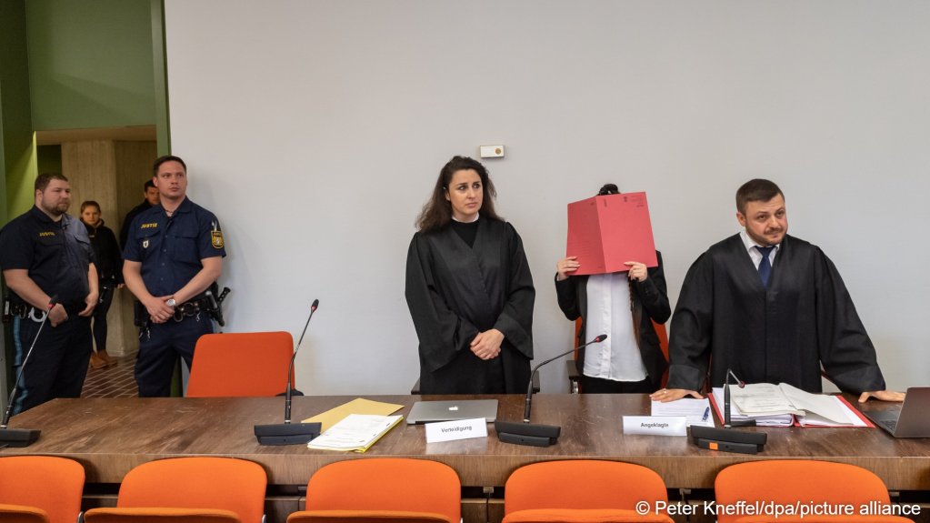 File photo: This case tried in Munich in 2019 involved accusations against the woman standing holding a red folder in front of her face of war crimes, being a member of a terrorist organization and having bought a little Yezidi girl as a slave | Photo: Peter Kneffel / dpa / picture alliance