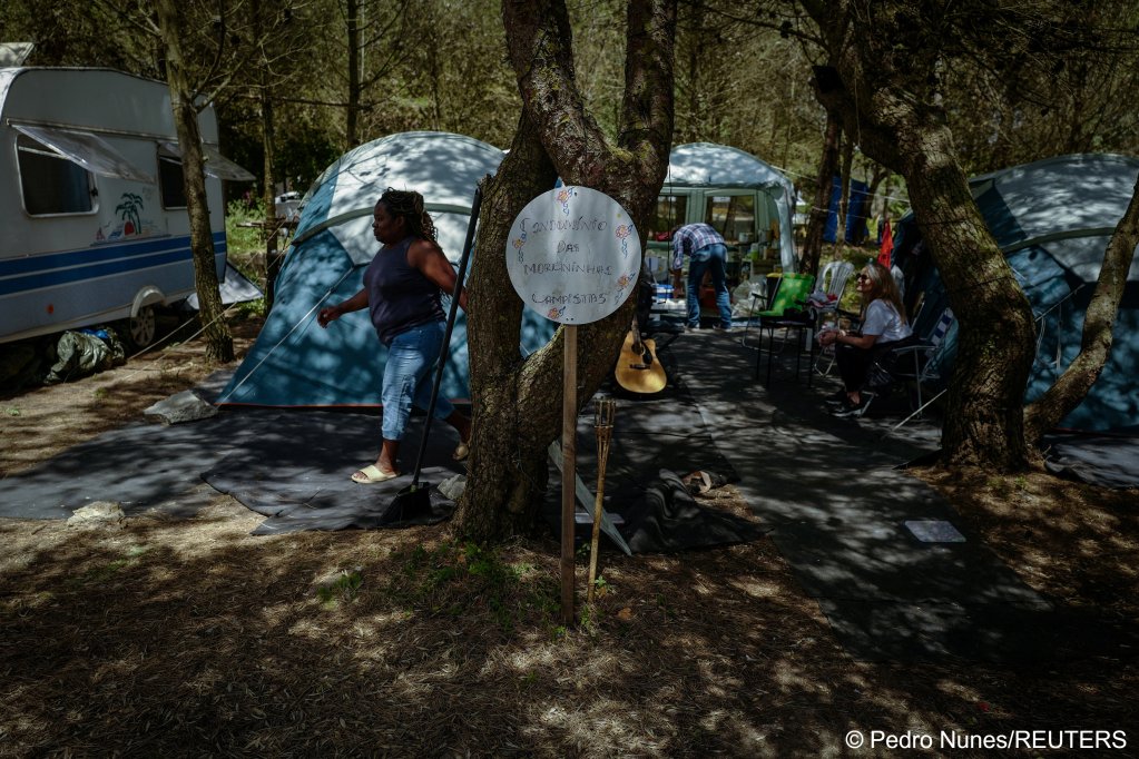 People gather at an improvised campsite in a field, ahead of their eviction from the campsite, near a sign which reads: 'The condominium of the dark-skinned campers,' in Carcavelos, in Cascais, Portugal, May 11, 2024. In Brazilian Portuguese, a 'moreninha' or 'morena' can be a white person with a tan and/or dark hair. It can also refer to a mixed race person or someone of African descent | Photo: Pedro Nunes / Reuters