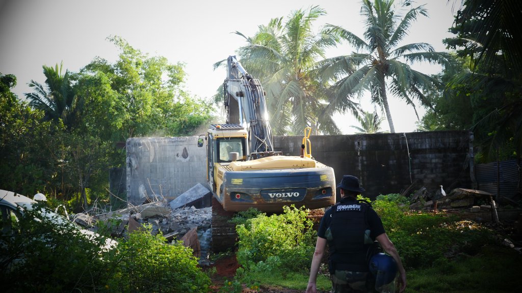Un gendarme passe devant une pelleteuse durant la démolition du bidonville de Longoni, à Mayotte, le 27 avril 2023. Crédit : Romain Philips pour InfoMigrants