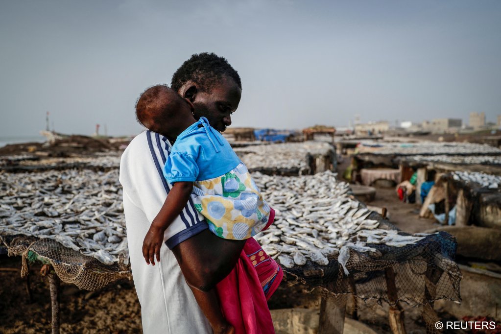 Fisherman Birane Mbaye, one of the survivors of a disastrous attempt to reach Spain last year, carries his 1-year-old daughter Maguette past drying fish in Fass Boye, Senegal, March 20, 2024 | Photo: REUTERS/Zohra Bensemra