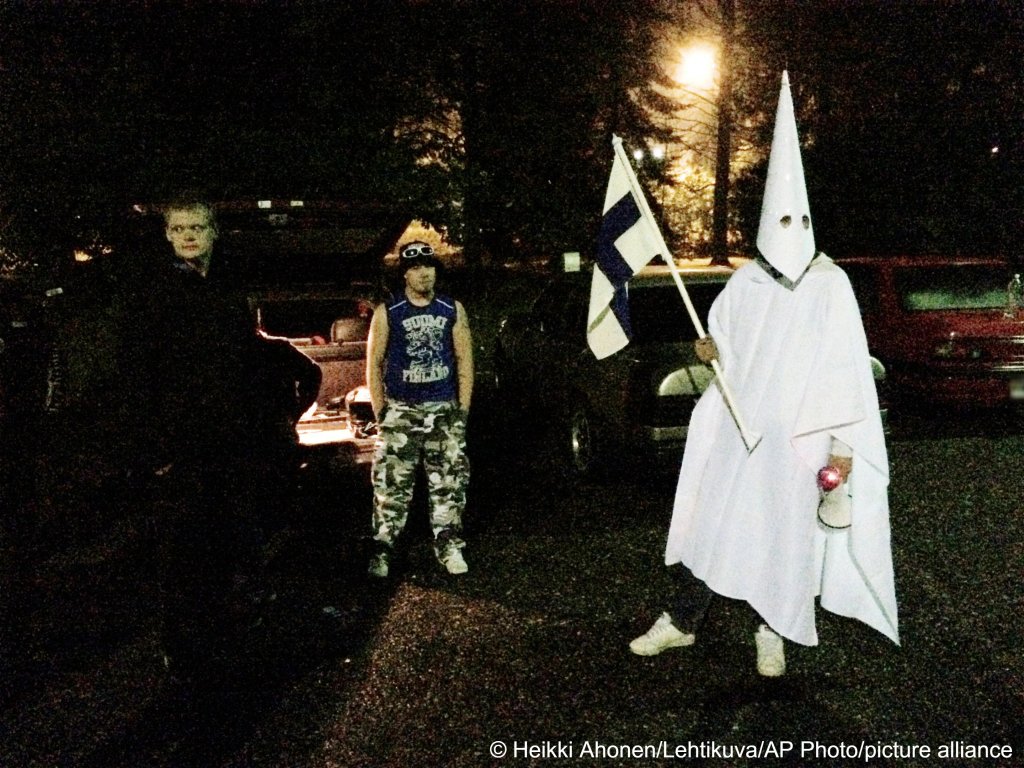 A group of demonstrators including one wearing an outft in the style of the Ku Klux Klan stand in protest against refugees near a former army barracks in Lahti, Finland on September 24, 2015 | Photo: Heikki Ahonen/Lehtikuva/AP/picture-alliance