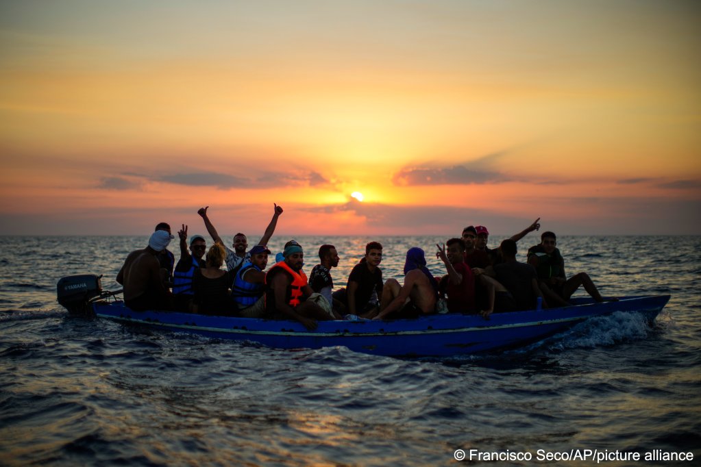 Migrants from Tunisia gesture as they sail in a wooden boat just before being assisted by crew members of the Spanish NGO Open Arms, sixteen miles west of the Italian island of Pantelleria | Photo: Francisco Seco / AP Photo/ picture alliance
