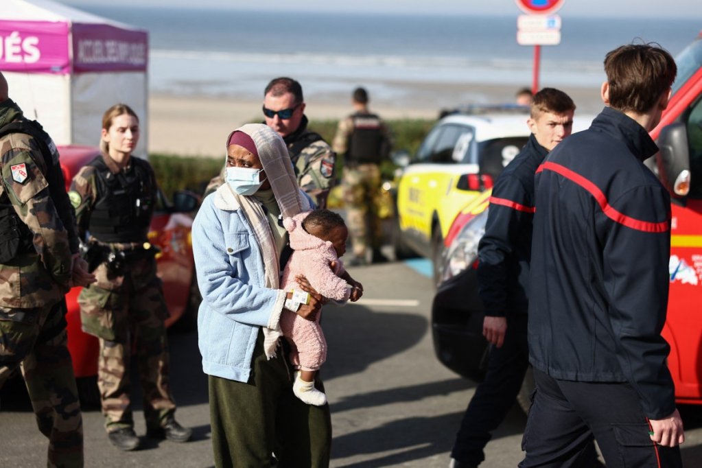 File photo: A woman with a baby stands alongside French rescuers after the deaths of four migrants during an attempt to cross the English Channel in Equihen-Plage, northern France on 9 April 2026. | Photo Crédit : AFP