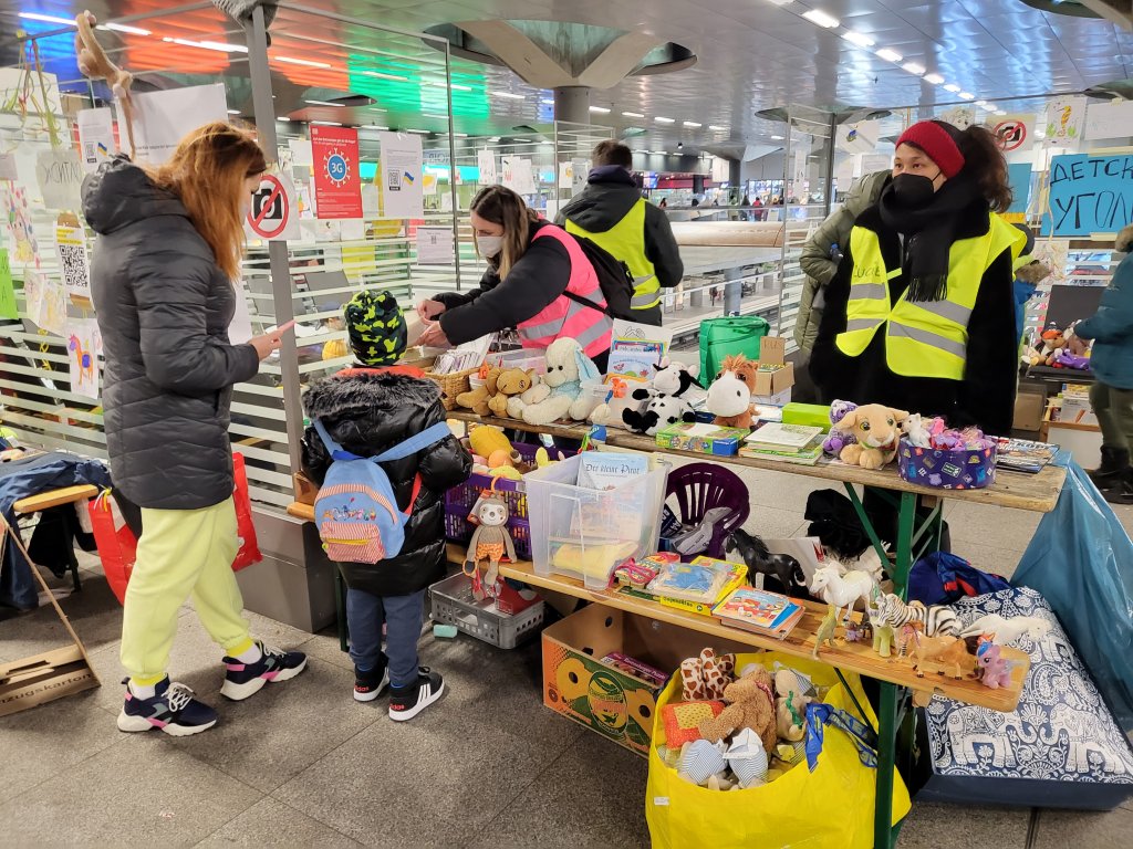 متطوعون يقدمون ألعابًا لطفل لاجئ داخل محطة القطار الرئيسية في برلين في 7 مارس 2022 | الصورة: بنيامين باثكه/ مهاجر نيوز