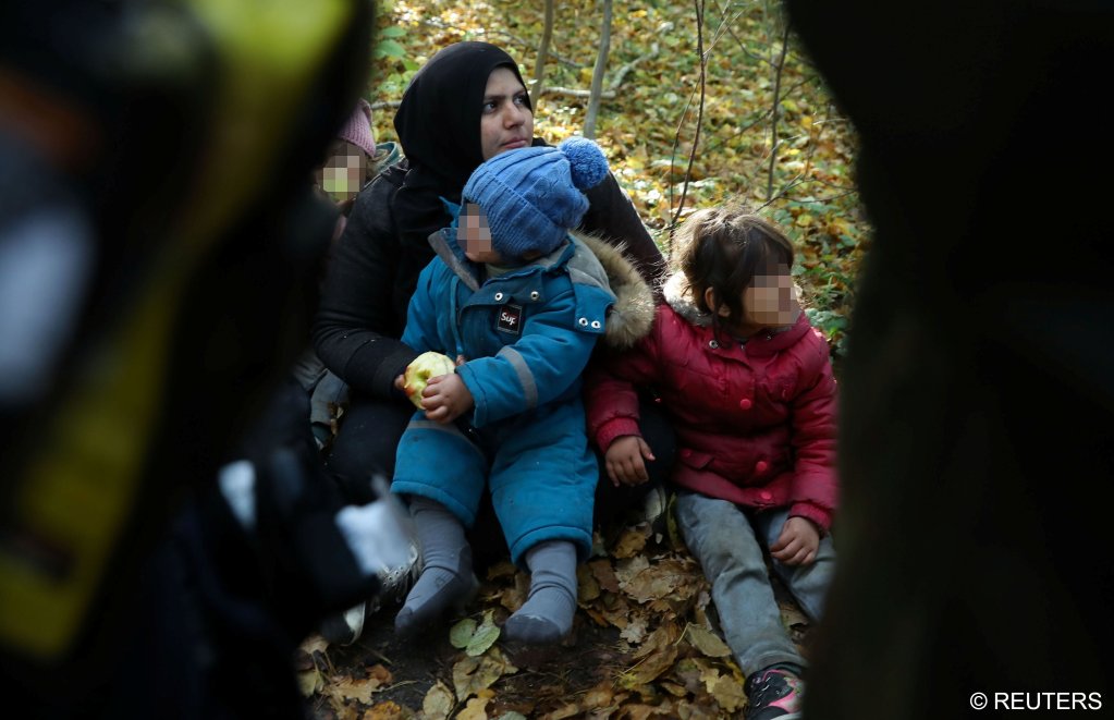 An Iraqi woman with children sits on the ground as they are surrounded by border guards and police officers after they crossed the Belarusian-Polish border | Photo: Reuters