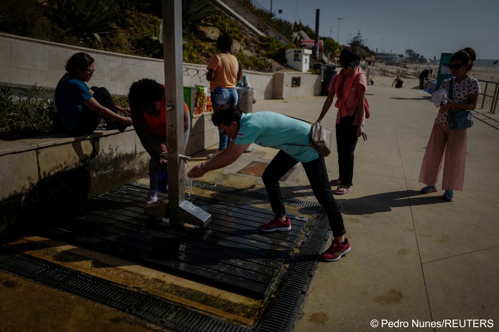 Marcia Leandro (2nd-L), 43, from Rio de Janeiro, Brazil and Andreia Costa (3rd-L), 50, from Sao Paulo, Brazil gather water at a beach shower to bring to the improvised campsite in a field where they live in Carcavelos, in Cascais, Portugal, October 11, 2023 | Photo: Pedro Nunes / Reuters
