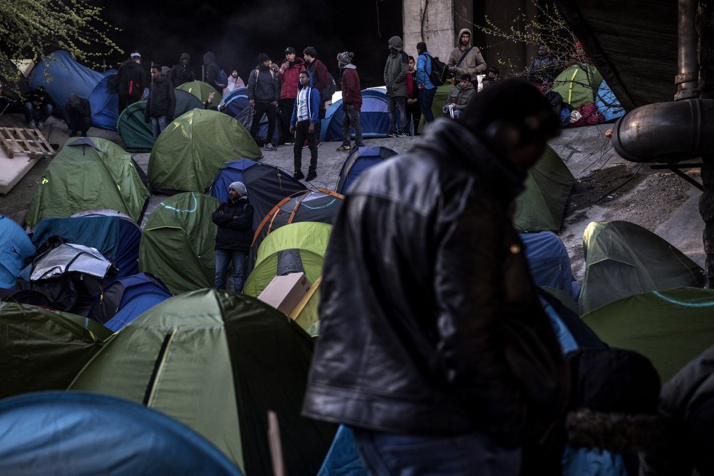 Migrants stand in front of tents as police and security agents (unseen) carry out an evacuation of a makeshift camp at Porte de la Chapelle, in the north of Paris, on April 4, 2019 | Photo: Christophe Archambault/AFP