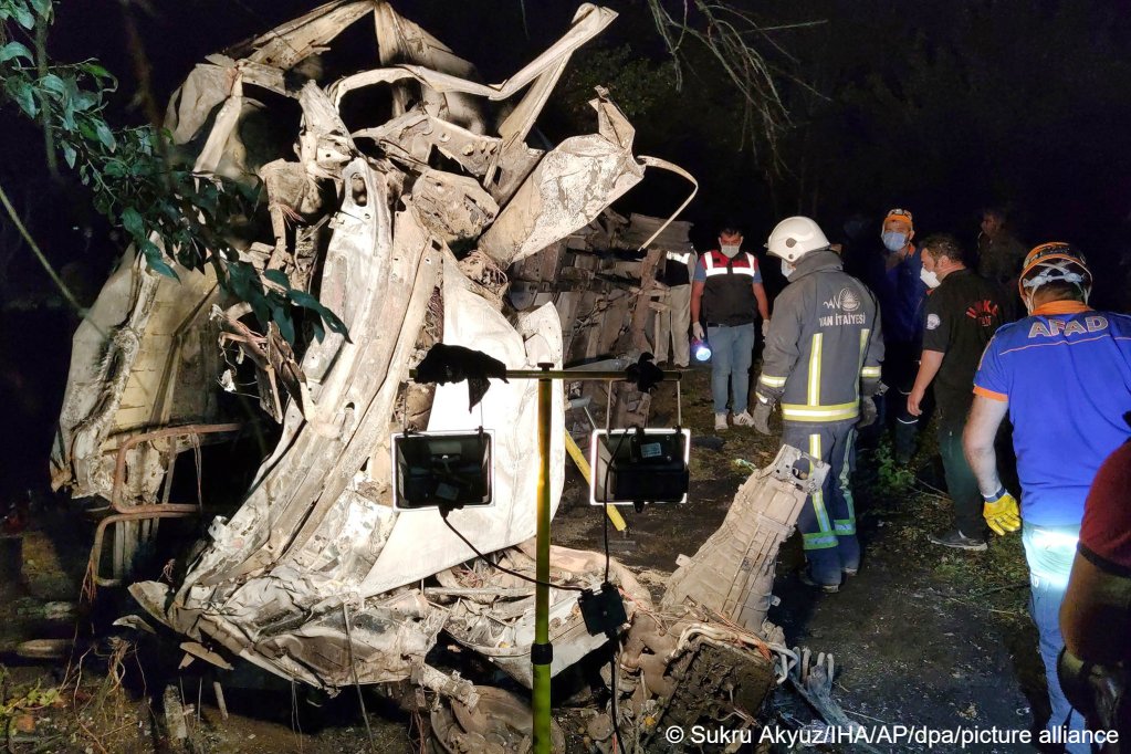 Emergency workers stand next to a burnt out minivan that crashed on July 11, 2021, in Van, eastern Turkey, killing at least 12 migrants | Photo: picture alliance/dpa/IHA/AP/Sukru Akyuz