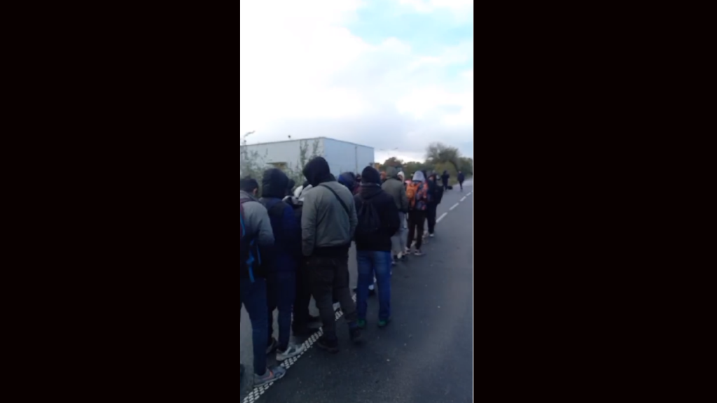 Migrants waiting for a bus at the exit to the camp at Loon Plage. According to Utopia 56, they waited but the buses never came | Photo: Screenshot from a video published by Utopia 56