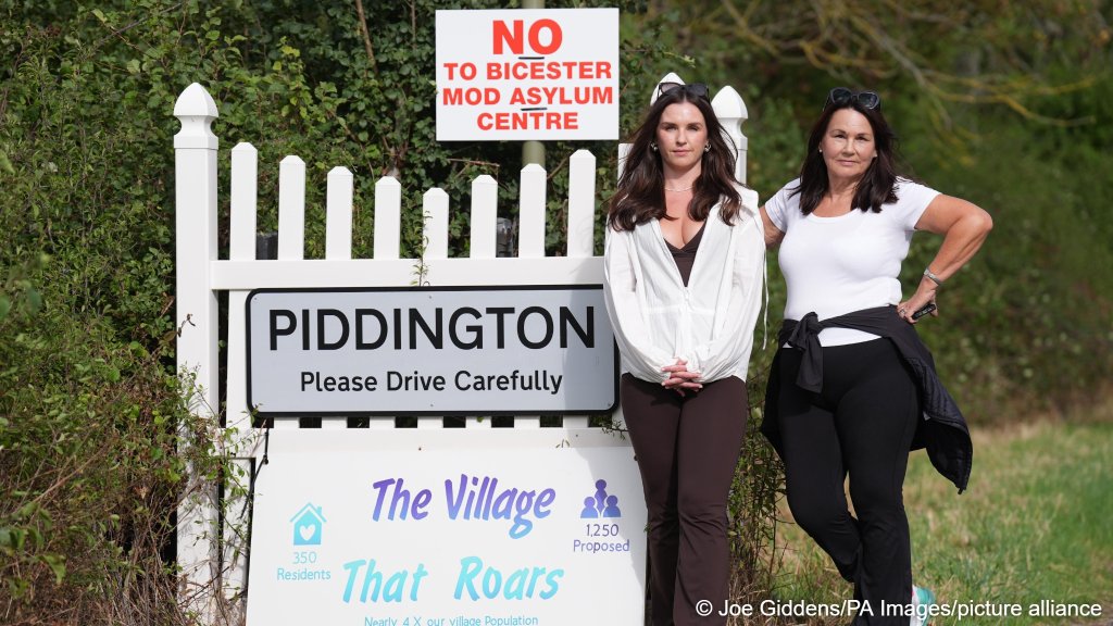 A mother and daughter who are village residents, stand beside a sign opposing the Bicester MOD Asylum Center | Photo: Joe Giddens/PA Wire