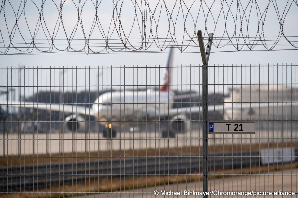 File photo: An airplane stands blurred in the background behind a barbed-wire fence at the airport, serving as a symbolic image of deportation and repatriation | Photo: picture alliance / CHROMORANGE