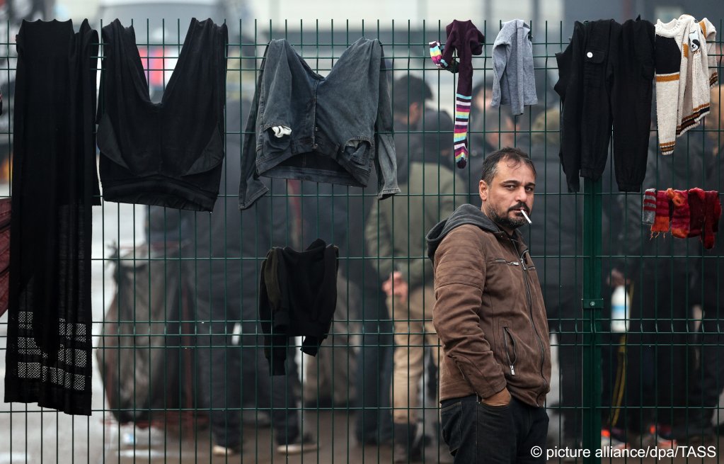  A refugee enjoys a cigarette by a fence on which clothes are drying at the Bruzgi Transport and Logistics Centre on November 22, 2021 | Photo: Sergei Bobylev/TASS/dpa/picture-alliance