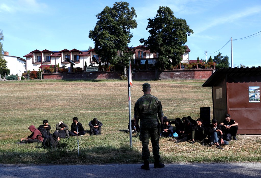 A Slovakian army soldier stands next to a group of migrants in the Slovakian village of Chl'aba on September 15, 2023; the migrants were detained after crossing the Slovakia-Hungary border irregularly | Photo: Bernadett Szabo/Reuters
